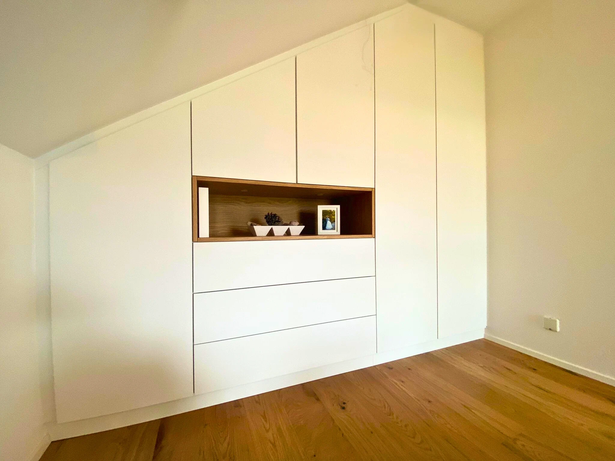 Maßgefertigter weißer Dachschrägenschrank mit beleuchteter Eichenholz-Nische, eingebaut von Schreinerei Mario Esch in Murrhardt – millimetergenaue Einpassung unter der Schräge.